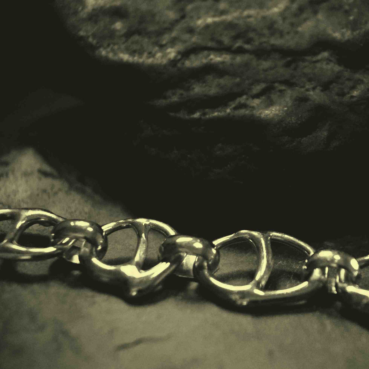 A close-up of a polished metal chain with interlocking oval links resting on a dark textured surface.