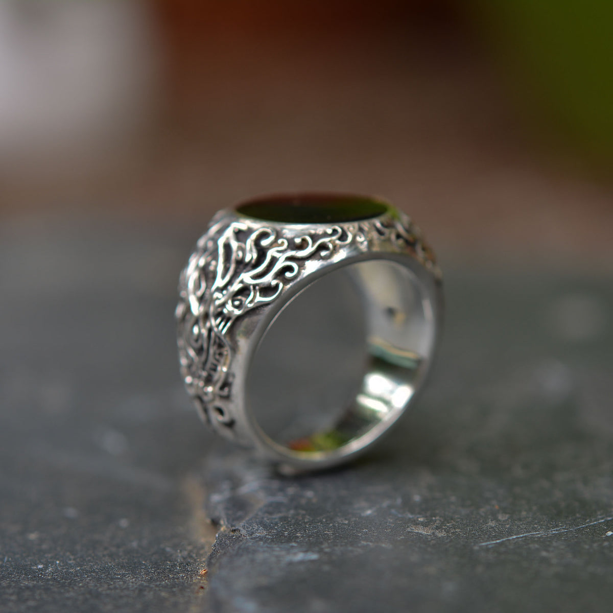 Silver ring with intricate designs on a textured surface.