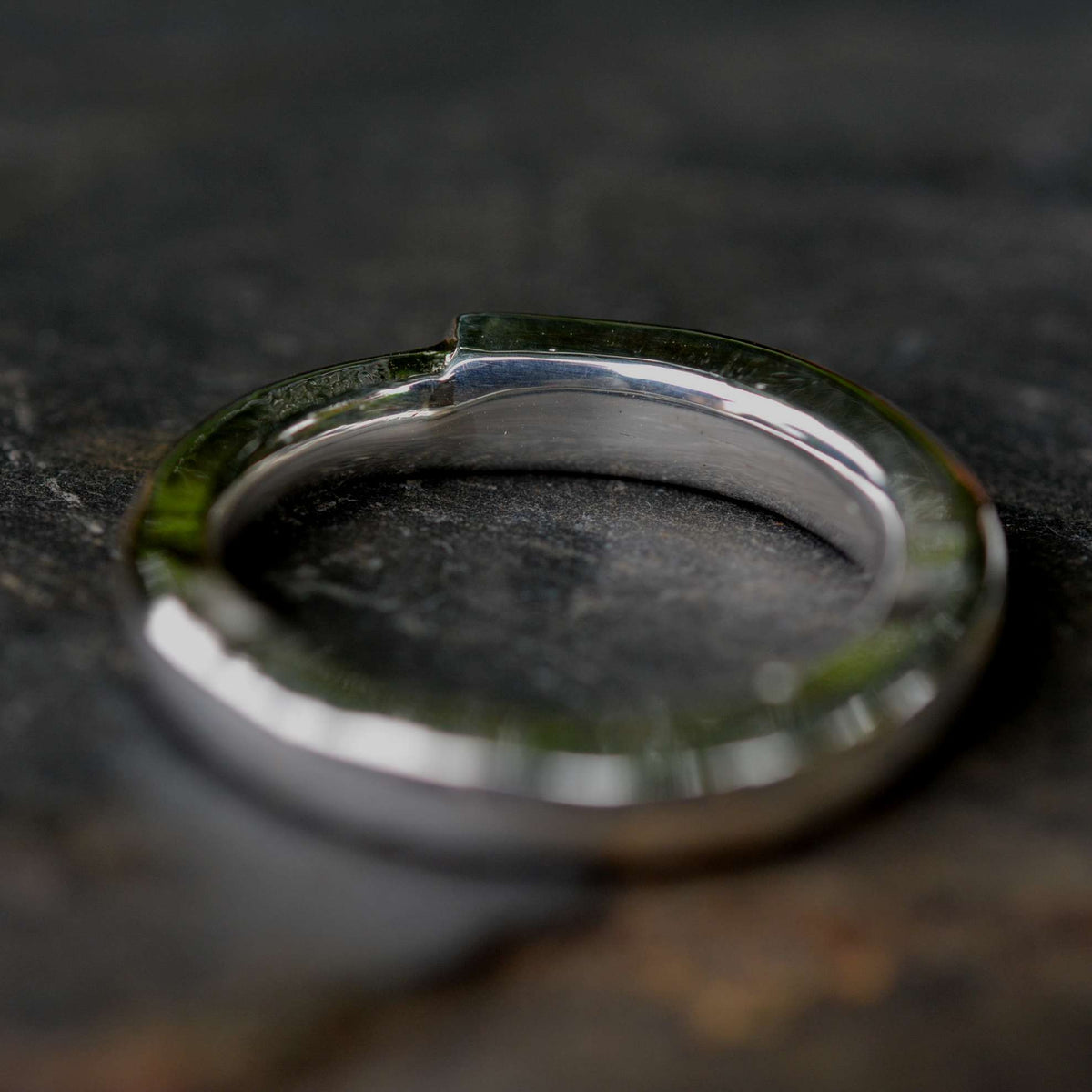 A close-up shot of a polished silver metal key ring with a small notch, resting on a dark, textured stone surface.