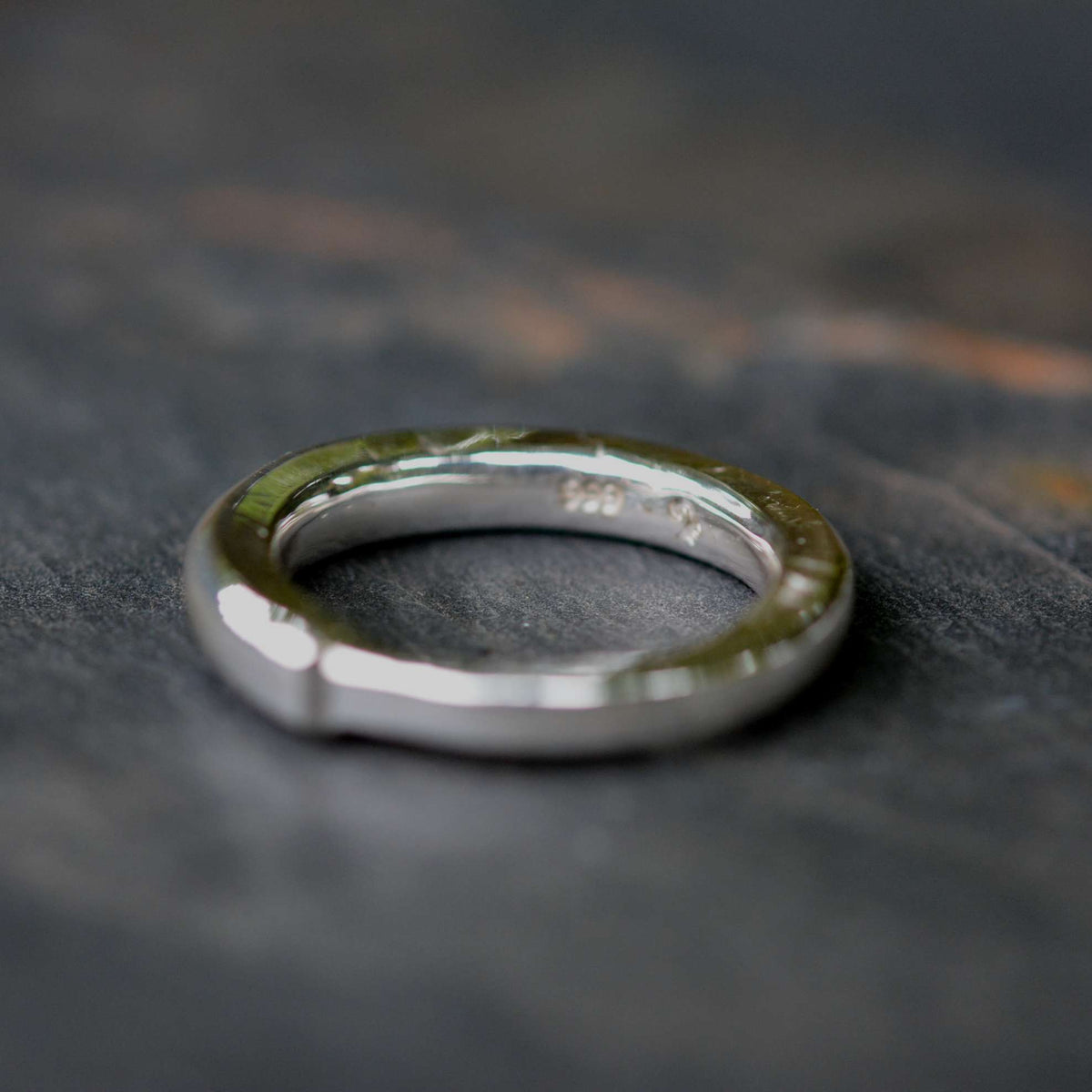 A polished silver metal ring with a textured, hammered finish on the outer band, resting on a dark, textured slate surface.