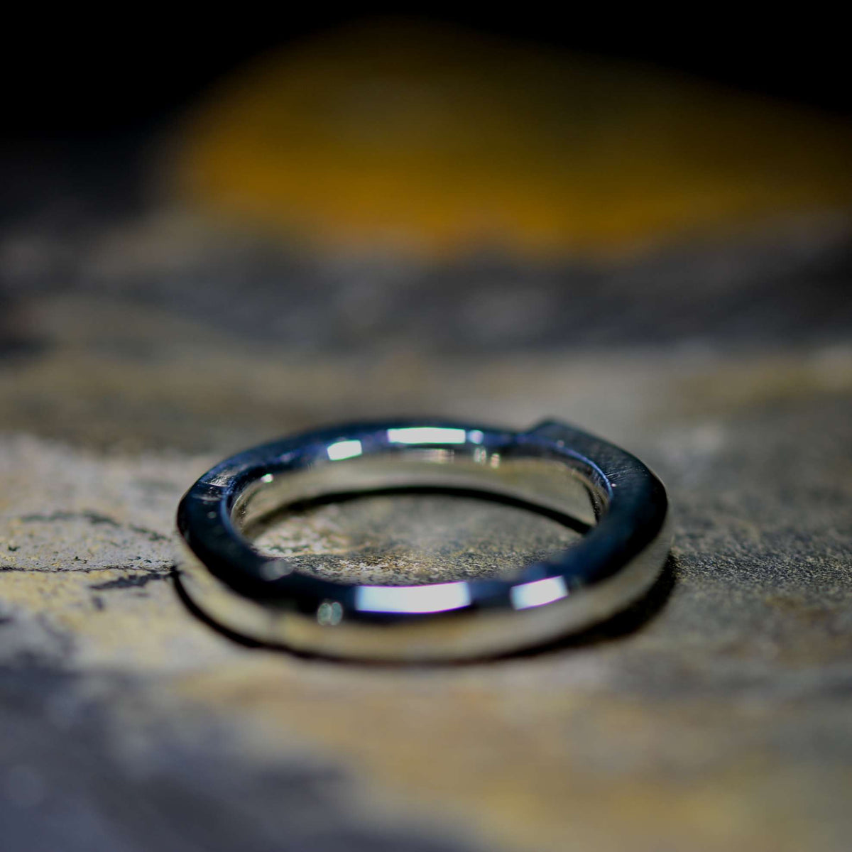 A polished silver metal ring with a thick, chunky band, resting on a textured stone surface with a dark, blurred background.