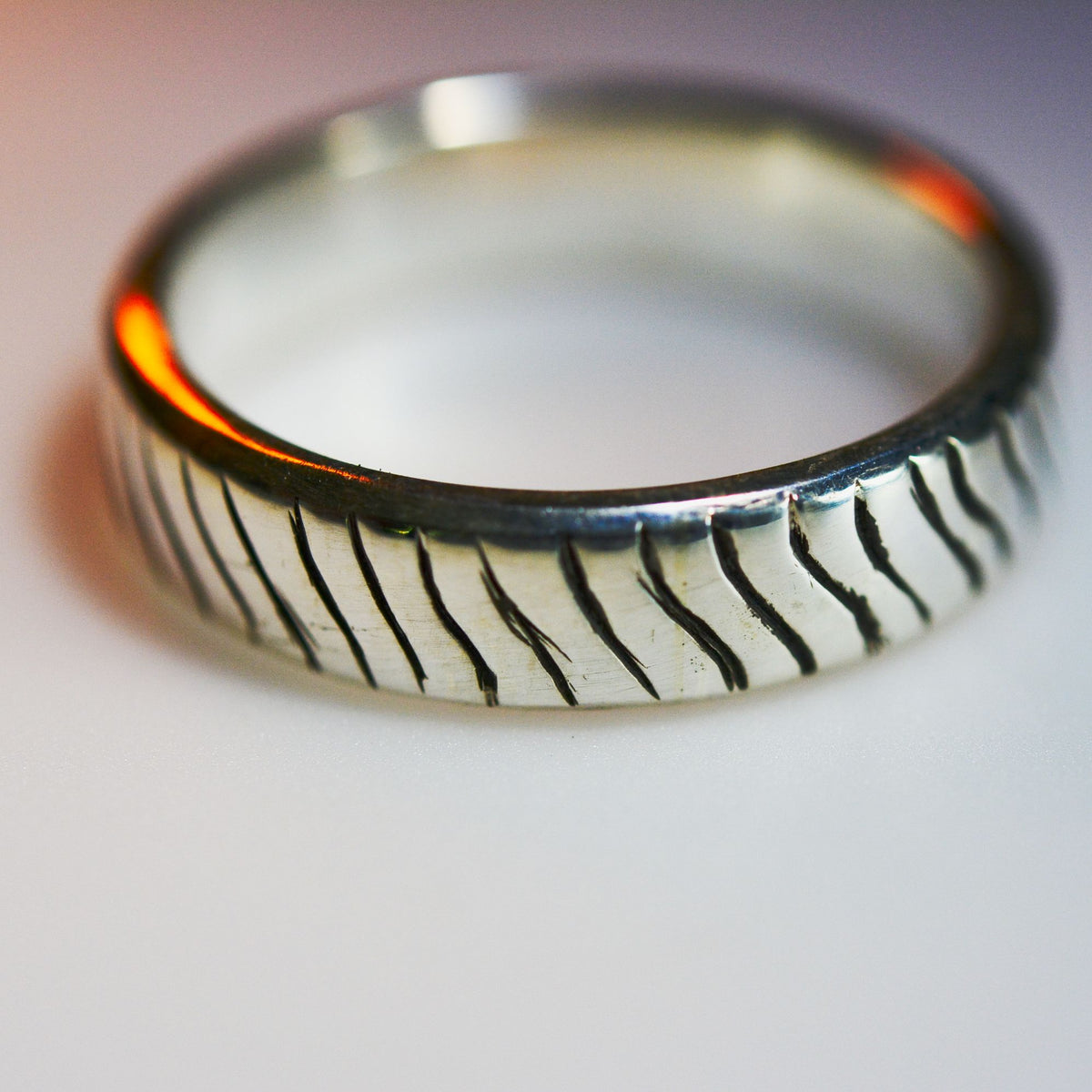 A silver band ring with a textured, vertically grooved exterior pattern, photographed on a neutral light gray background.