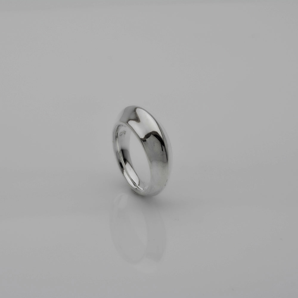 A polished silver band ring standing upright on a light gray reflective surface.
