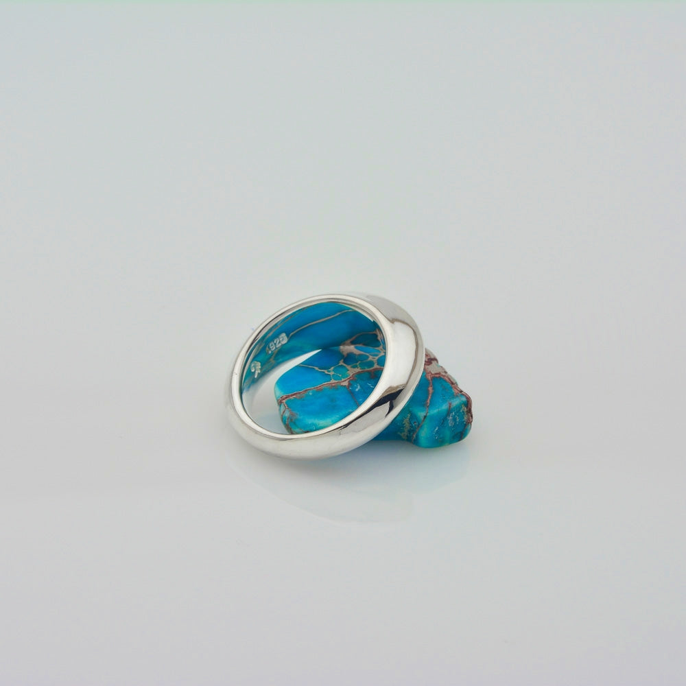 A sterling silver ring with a large, rounded bezel-set turquoise stone showing natural brown matrix veining, displayed on a clean light gray background.