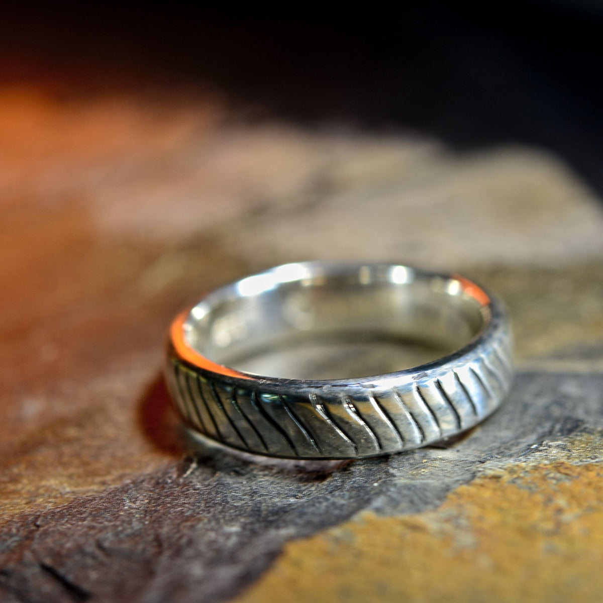 A silver-toned textured ring with a ribbed, grooved pattern, resting on a rustic, warm-toned stone surface.