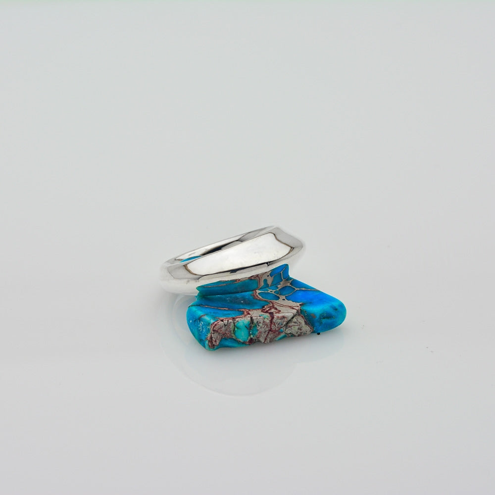 A silver ring with a flat, polished band and a rectangular turquoise stone featuring brown and reddish matrix patterns, displayed on a clean white surface.