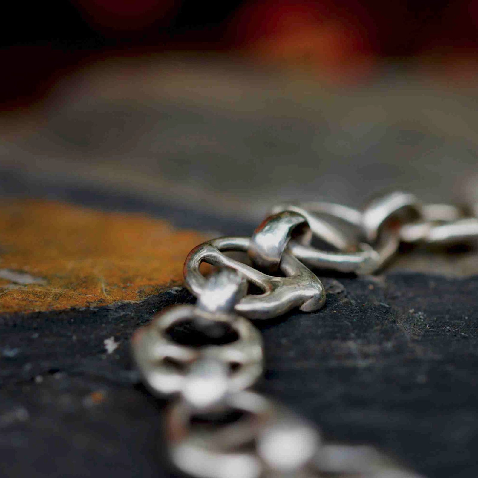 A silver-tone chain bracelet made of interlocking pull-tab style links, photographed on a dark textured surface with a yellowish stone patch in the upper left.